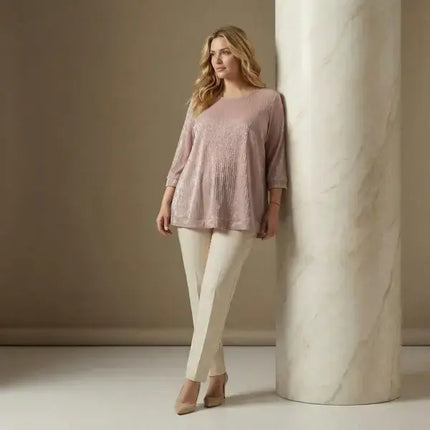 Жена с елегантна туника в размер 4XL в пудра розов цвят комбинирана със светъл панталон в студио с мек неутрален фон и колона