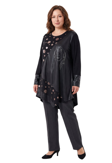 Жена, облечена в черна асиметрична туника с панели на точки и блестяща апликация с лице, позира на бял фон.