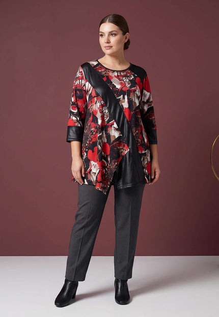 Асиметрична дамска макси туника с абстрактен десен в червено и черно и кожени детайли, представена в цял ръст със сив панталон.