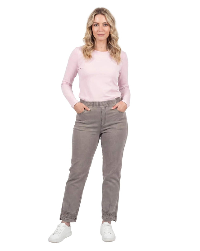 Бежови дамски дънки големи размери с права кройка и декорация от камъчета по крачолите. Показани в цял ръст на бял фон, съчетани с розова блуза.