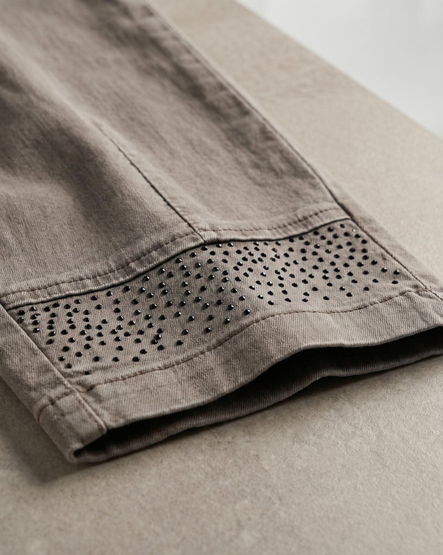 Детайл отблизо на долната част на крачола на бежови дамски дънки, акцентиращ върху красивата декорация от черни блестящи камъчета.