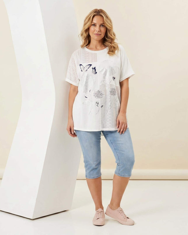 Бяла лятна памучна туника големи размери с флорална апликация и дантела върху манекен, заснета в цял ръст.
