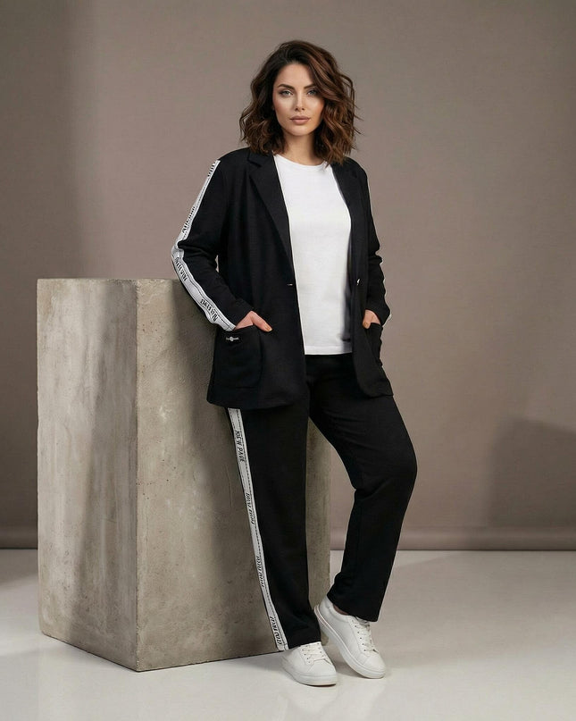 Ежедневен черен дамски комплект от сако и панталон с бели кантове по дължината, представен в цял ръст до сив декоративен блок.