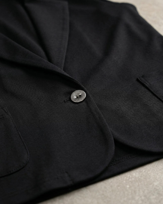Детайл отблизо на черно дамски сако от комплект големи размери, показващ закопчаването с едно копче, джобовете и еластичната материя.