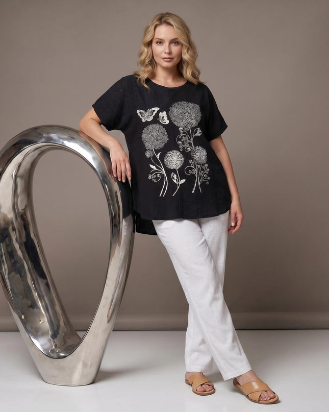Черна лятна макси туника с ефектна сребриста апликация на цветя и пеперуди. Кадър в цял ръст на модел, съчетал туниката с бели панталони.