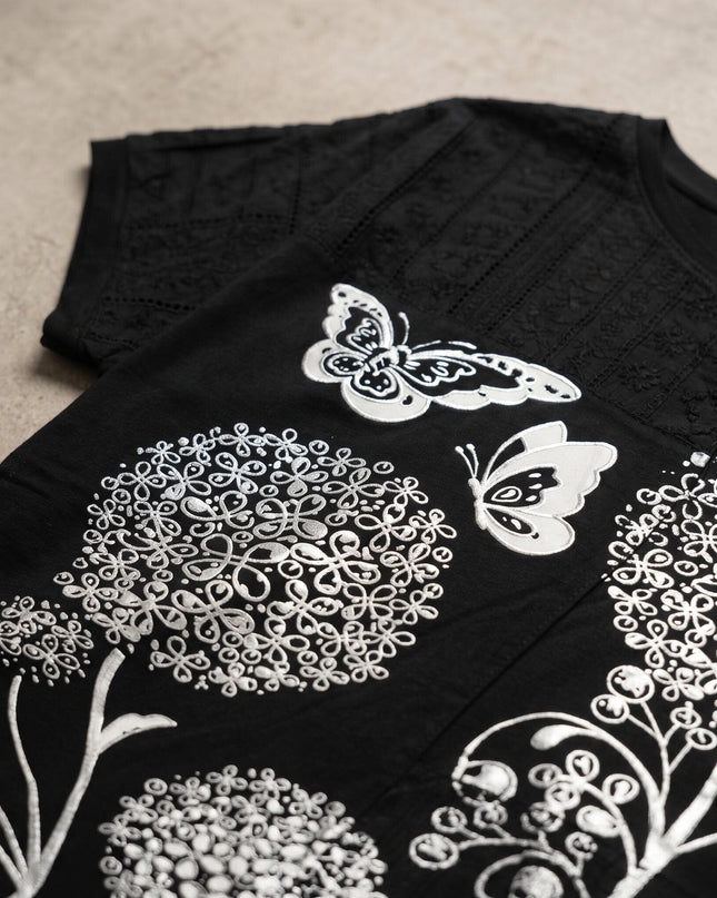 Детайл отблизо на черна лятна макси туника, открояващ красивата сребриста апликация на цветя и пеперуди, както и елементите от черна дантела.