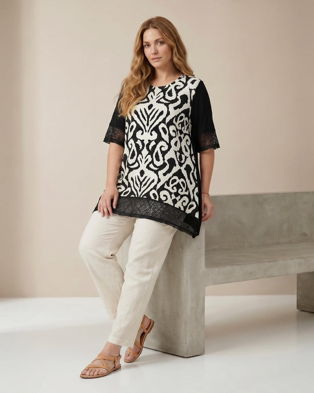 Черна лятна туника големи размери с абстрактен принт и мрежести детайли по ръкавите и подгъва. Моделът е показан в цял ръст, облечен със светъл панталон.