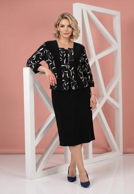 Черна официална рокля големи размери с бял листен мотив в горната част и ефектна брошка, заснета в цял ръст.