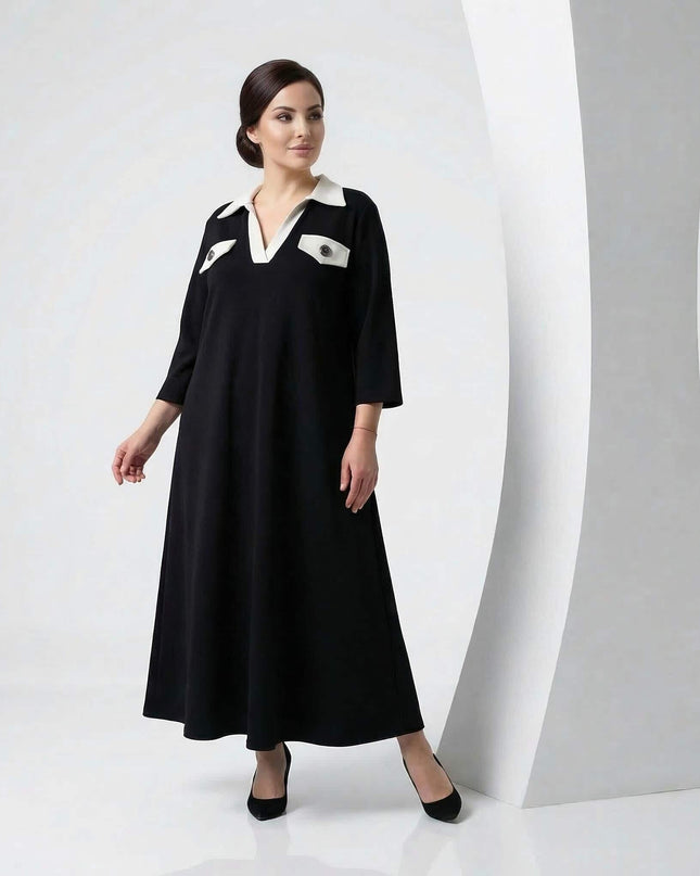 Елегантна черна макси рокля големи размери с бяла контрастна яка и джобове. Моделът е представен в цял ръст на светъл студиен фон.