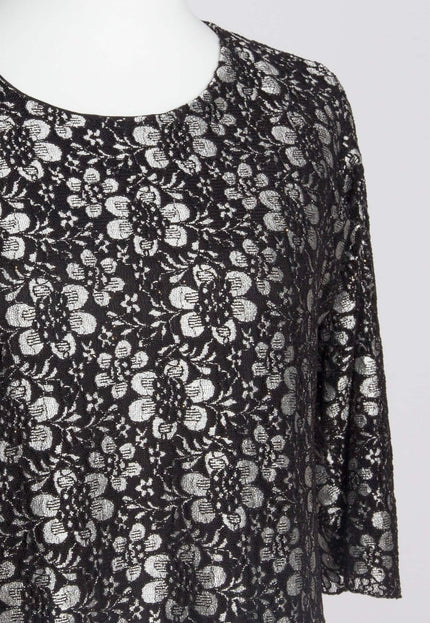 Детайлен кадър на черна официална рокля с флорална дантела, фокусиран върху облото деколте и красивите сиви цветя върху черната материя.