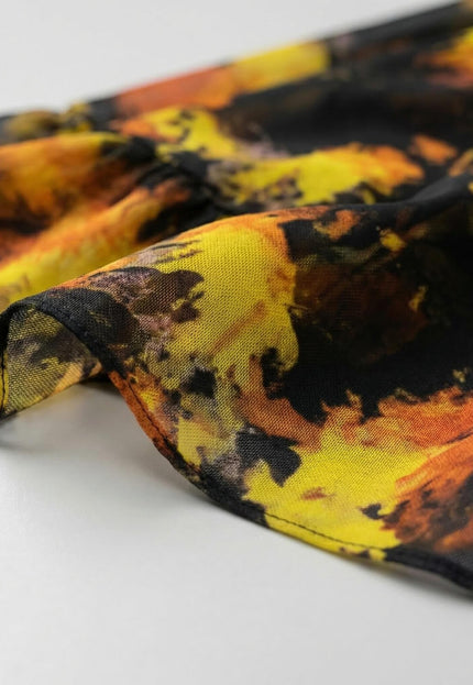 Детайл отблизо на ефирната материя на черна официална шифонена рокля с абстрактен принт в топли жълти и оранжеви нюанси.