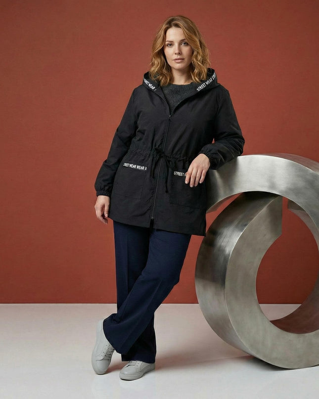 Черна разкроена макси ветровка с качулка и джобове, представена в цял ръст с акцент върху връзките на талията и декоративните надписи.