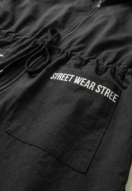 Детайл отблизо на черна макси ветровка, изобразяващ джоб с декоративен надпис Street Wear и връзки за регулиране на талията.