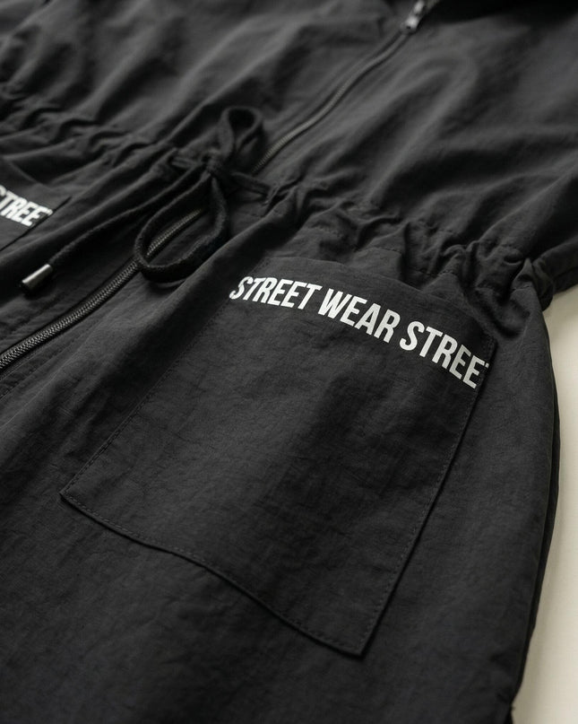 Детайл отблизо на черна макси ветровка, изобразяващ джоб с декоративен надпис Street Wear и връзки за регулиране на талията.
