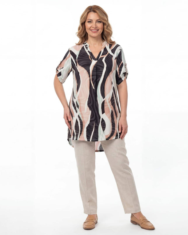 Дълга лятна макси туника с шарен абстрактен принт и V-образно деколте. Представена в цял ръст на бял фон, съчетана с бежов панталон.