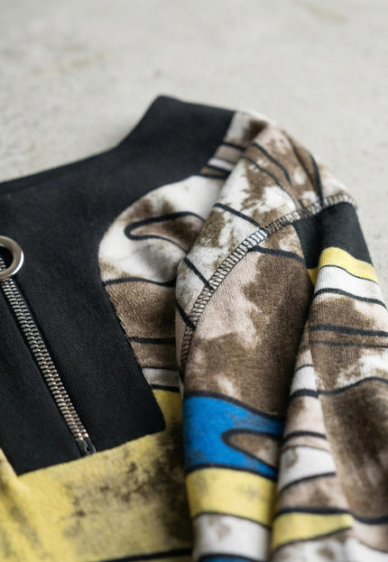 Детайл отблизо на метален цип с халка и абстрактен шарен десен на дълга макси туника, показващ текстурата на меката материя и шевовете.