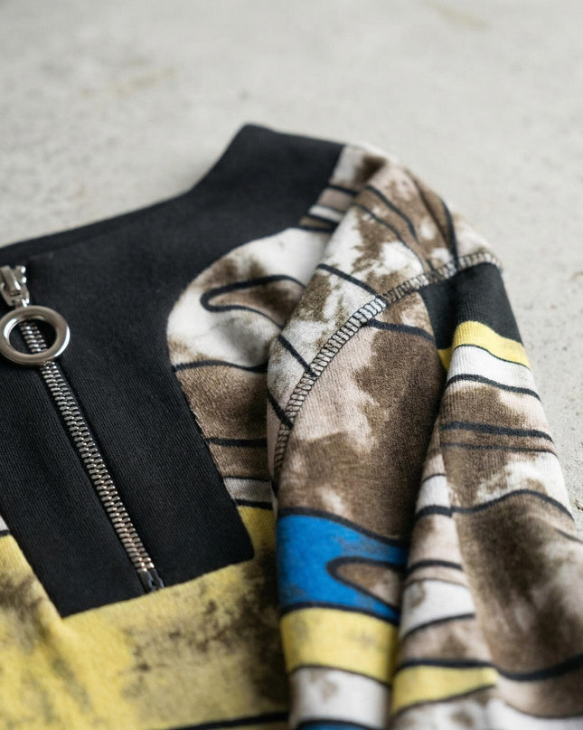 Детайл отблизо на метален цип с халка и абстрактен шарен десен на дълга макси туника, показващ текстурата на меката материя и шевовете.