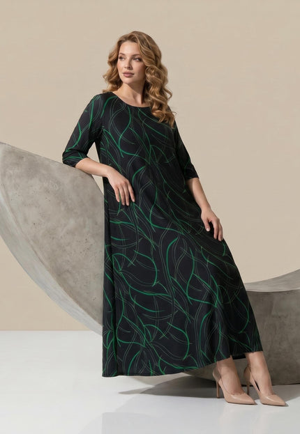 Дълга официална макси рокля в черно със зелен линеен принт. Кадър в цял ръст на седнал модел, показващ разкроения силует на дрехата.