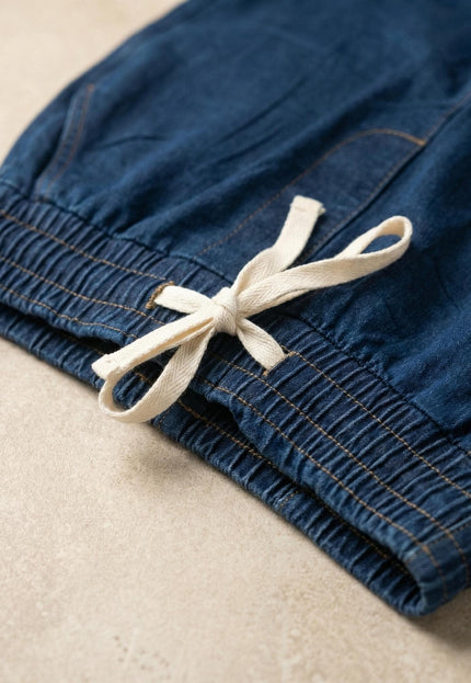 Детайл отблизо на дамски еластични дънки в син цвят, показващ удобния ластик в талията и бели връзки на плосък кадър.