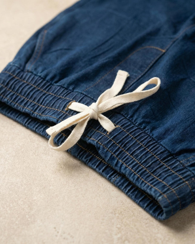 Детайл отблизо на дамски еластични дънки в син цвят, показващ удобния ластик в талията и бели връзки на плосък кадър.