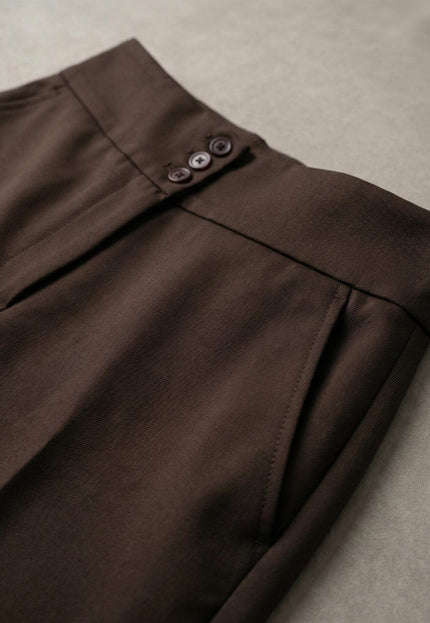Детайлен кадър на елегантен кафяв панталон с висока талия, показващ акцента с три копчета, страничния джоб и фината текстура на плата.