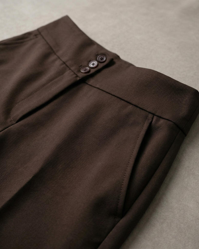 Детайлен кадър на елегантен кафяв панталон с висока талия, показващ акцента с три копчета, страничния джоб и фината текстура на плата.