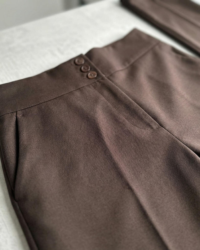 Детайл отблизо на колана с три копчета и страничния джоб на елегантен кафяв панталон с висока талия, заснет в плосък кадър.
