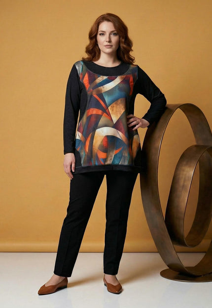 Елегантна дамска туника в черно с цветен витражен принт отпред. Моделът позира в цял ръст, демонстрирайки свободната А-образна кройка и дългите ръкави.