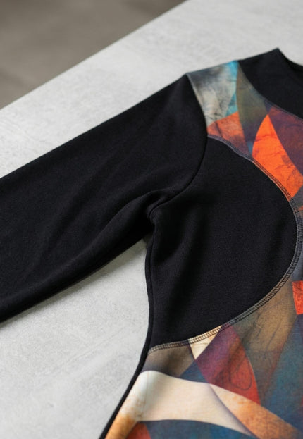 Детайлен кадър на елегантна есенна туника с витражен принт, показващ черния дълъг ръкав, облото деколте и връзката с цветния преден панел.