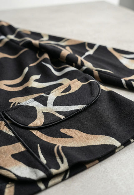 Детайл отблизо на елегантно черно макси сако с абстрактен десен, акцентиращ върху декоративния джоб и текстурата на меката материя.