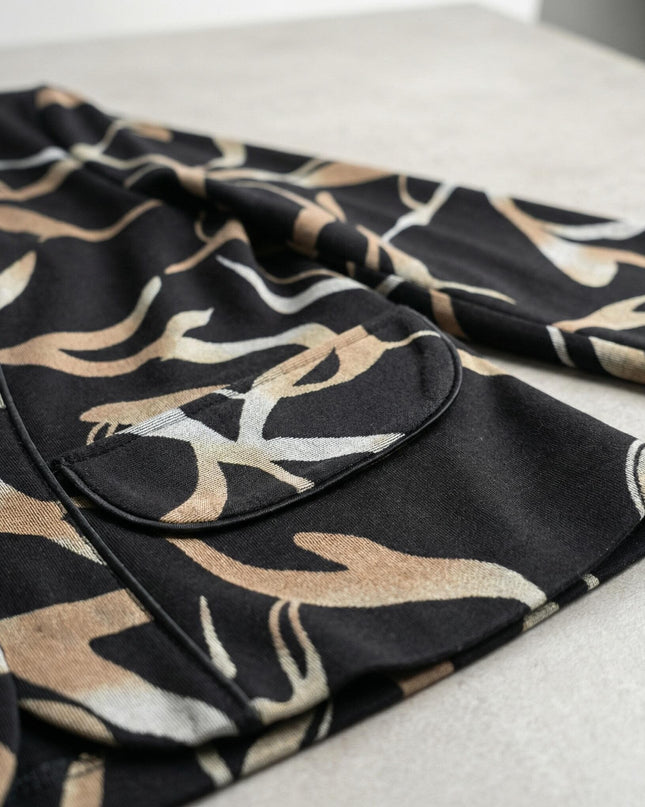 Детайл отблизо на елегантно черно макси сако с абстрактен десен, акцентиращ върху декоративния джоб и текстурата на меката материя.