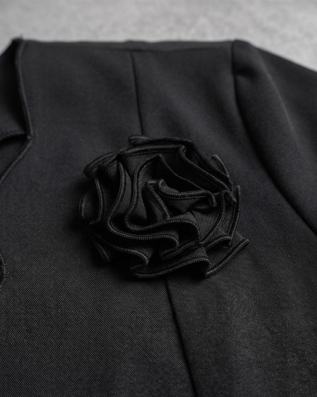 Детайл отблизо на елегантно черно сако, показващ ефектната текстилна 3D роза и нежния вълнообразен ръб по деколтето.