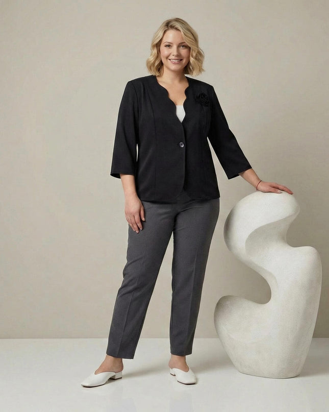 Елегантно черно сако големи размери с акцент 3D роза и 3/4 ръкави, представено в цял ръст върху модел в съчетание със сив панталон.