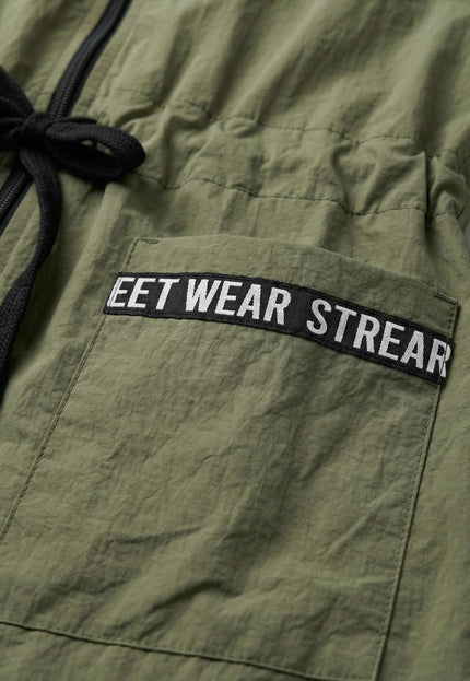 Детайлен кадър отблизо на джоб с декоративен надпис и черни връзки на талията върху дамска ветровка в цвят каки.