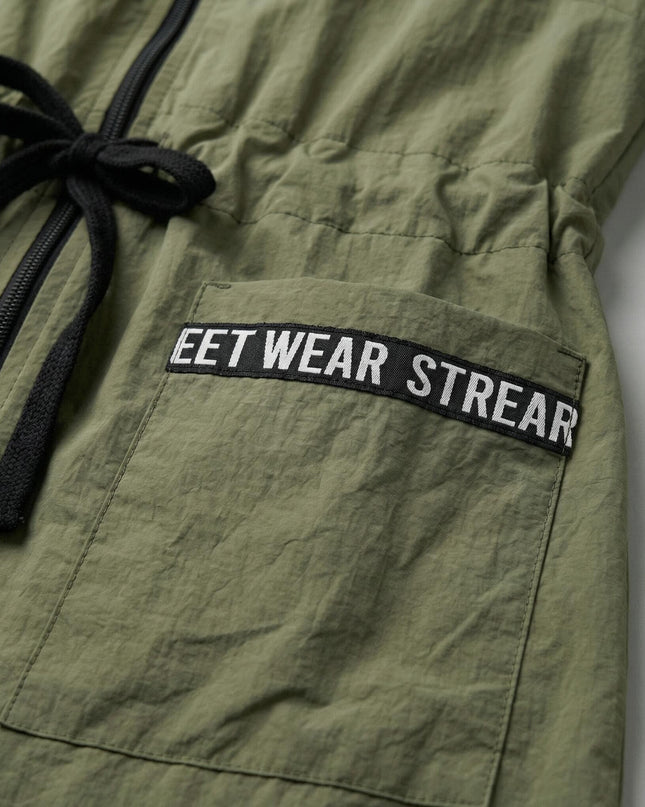 Детайлен кадър отблизо на джоб с декоративен надпис и черни връзки на талията върху дамска ветровка в цвят каки.