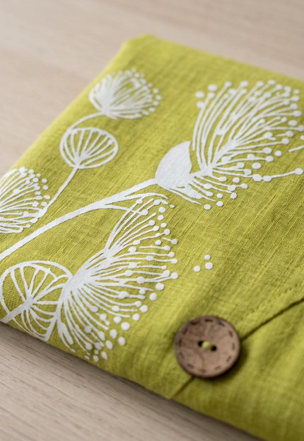 Детайл отблизо на зелена памучна макси рокля с бяла флорална щампа тип глухарче и декоративно дървено копче.