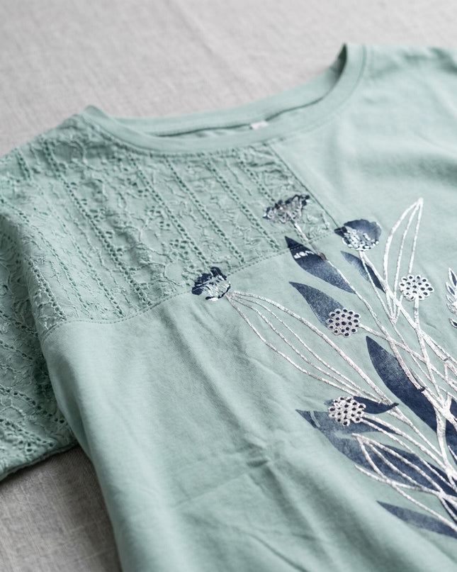 Детайл отблизо на ежедневна памучна туника в зелено, показващ дантелени панели и ефектна флорална апликация със сребристи акценти.