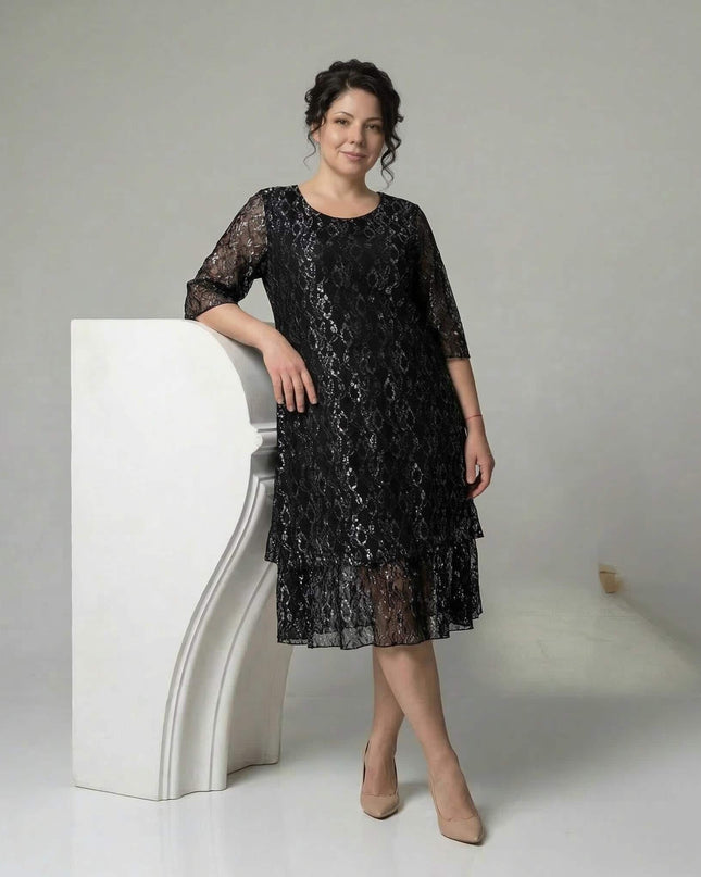 Официална черна макси рокля с ефектна дантела, разкроена кройка с етажиран подгъв и 3/4 дантелени ръкави. Моделът е в цял ръст, позиращ до бял пиедестал.