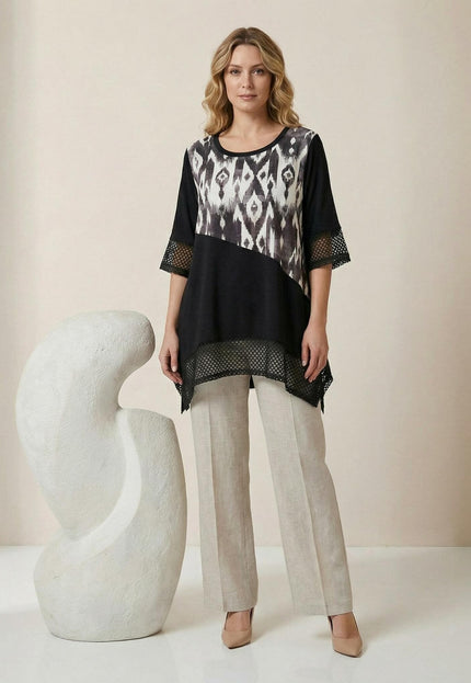 Официална черна макси туника с диагонален принт и асиметрична кройка с мрежа, показана в цял ръст върху модел, съчетана със светъл панталон.