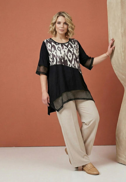Официална черна макси туника с абстрактен принт и мрежести акценти, показана в цял ръст в съчетание с елегантен светъл панталон.