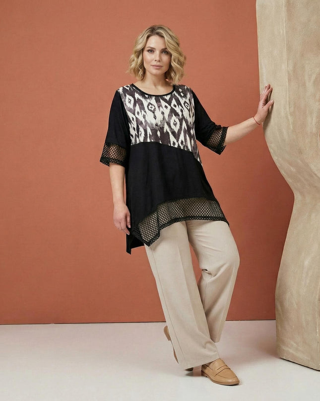 Официална черна макси туника с абстрактен принт и мрежести акценти, показана в цял ръст в съчетание с елегантен светъл панталон.