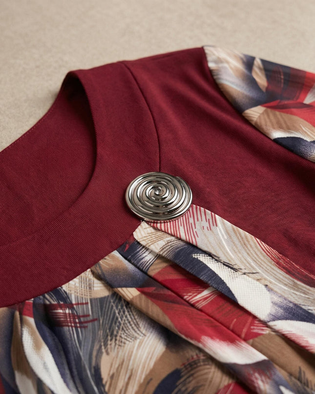 Детайлен кадър на деколтето на официална червена туника с флорален шифон, акцентиращ върху стилна сребриста брошка със спираловидна форма.