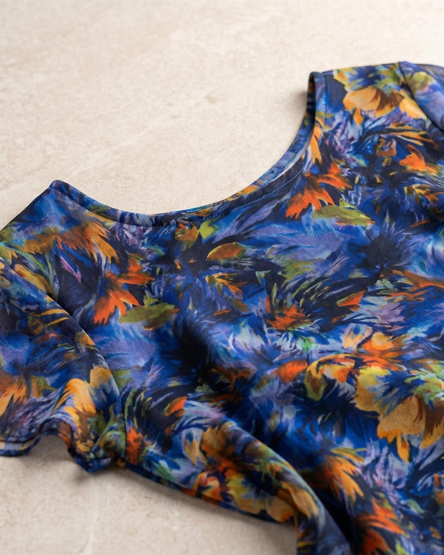 Детайл отблизо на официална макси рокля от пъстър шифон. Плосък кадър, показващ деколтето и ефирната материя с абстрактен флорален принт.