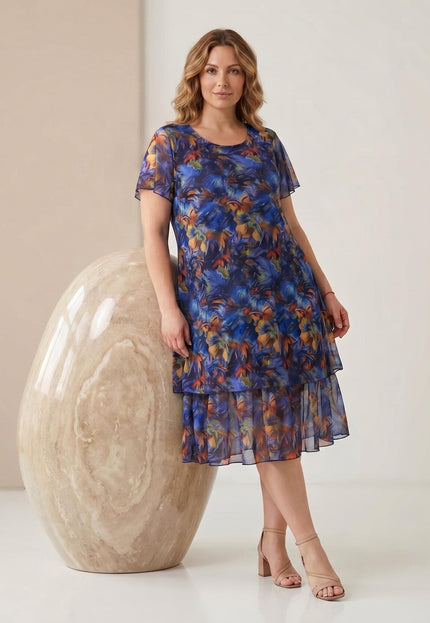 Официална макси рокля от пъстър шифон с разкроен силует, къси ръкави и флорален принт. Представена в цял ръст до голям декоративен камък.