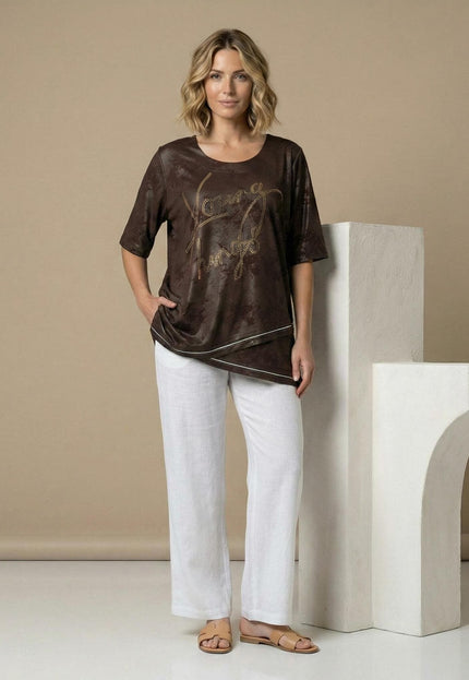 Официална макси туника в кафяво с асиметрична кройка и надпис от камъчета. Снимка в цял ръст, представена в комбинация с бял панталон.