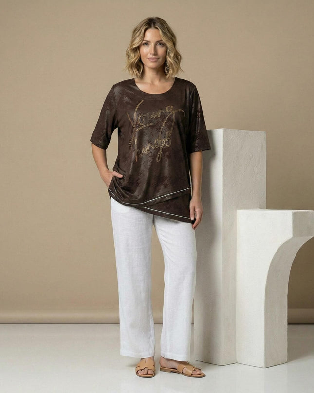 Официална макси туника в кафяво с асиметрична кройка и надпис от камъчета. Снимка в цял ръст, представена в комбинация с бял панталон.