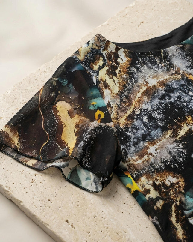 Детайл отблизо на официална рокля от шифон, показващ къс разкроен ръкав, обло деколте и красив шарен абстрактен принт.