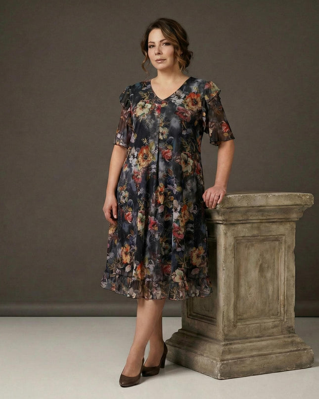 Официална разкроена рокля от шифон с живописен флорален принт, V-образно деколте и волан, заснета в цял ръст до декоративна колона.