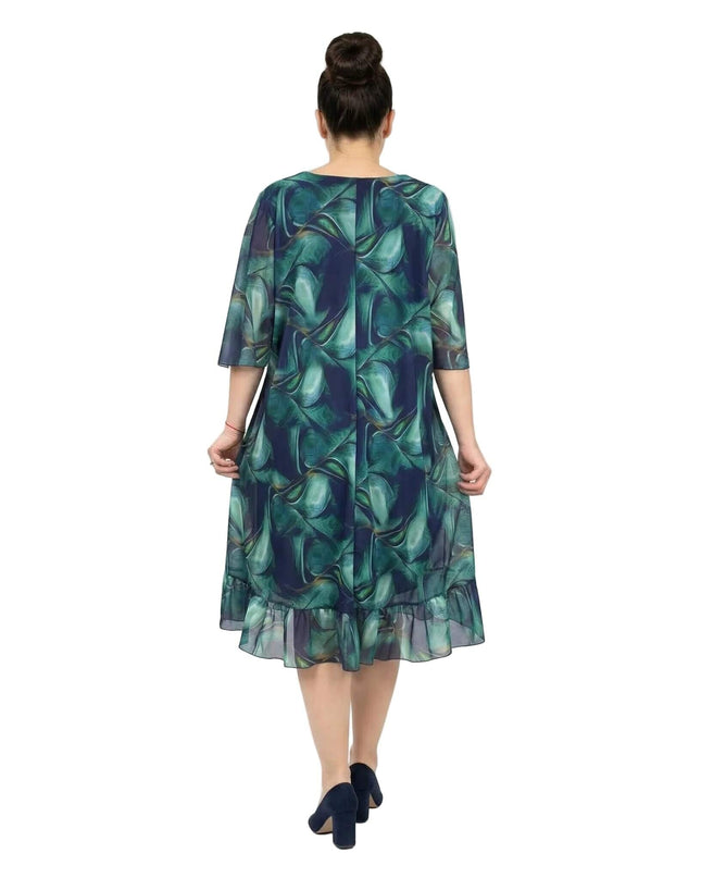 Официална шифонена рокля големи размери в преливащи сини тонове, заснета отзад в цял ръст на бял фон, показваща широките ръкави и волана на подгъва.