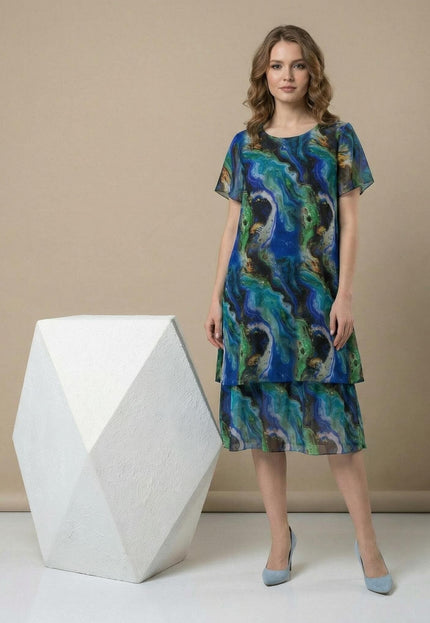 Официална шифонена рокля големи размери в синьо-зелени преливащи тонове. Визия в цял ръст, подчертаваща многопластовия дизайн и облото деколте.